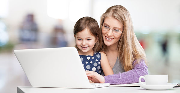 Studierende mit Kind arbeitet am Laptop, beide lächeln.