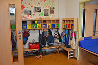 Day care center - checkroom. Left and right a door. Clothes and backpacks hang on the coat hooks. The wall is colorfully painted, photos are hung.
