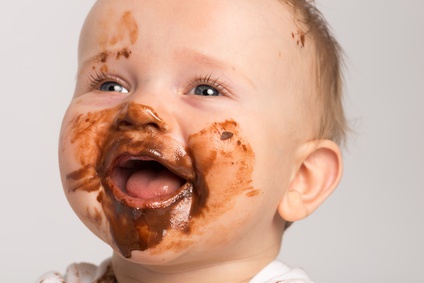 Portrait eines lachenden Babys, der Mund und das halbe Gesicht sind mit Schokolade verschmiert