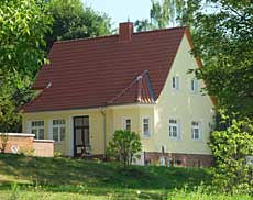 Gebäude 13 - Ein gelbes Haus mit rotem Ziegeldach, umgeben von Bäumen