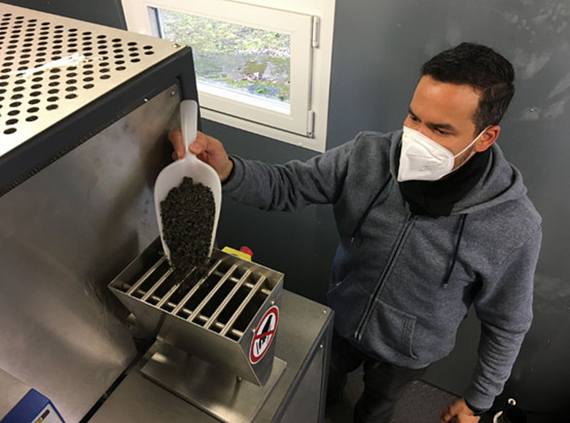 Materialaufgabe - ein junger Mann trägt eine weiße FFP2-Maske und füllt schwarzes Granulat in einen Trichter