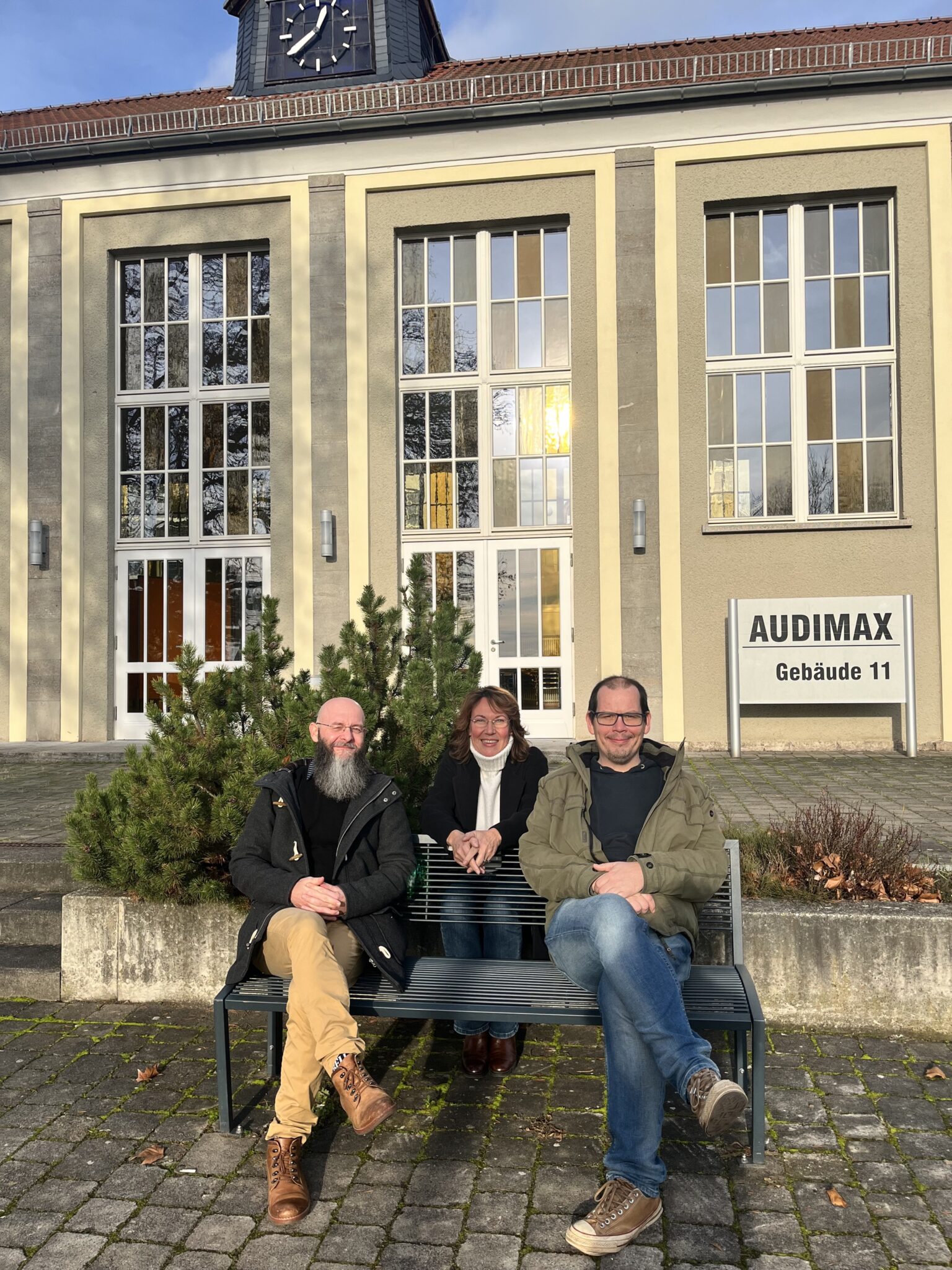 Drei Personen vor einem Gebäude.