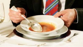 Nahaufnahme einer Person in beim Essen einer Suppe an einem gedeckten Tisch.