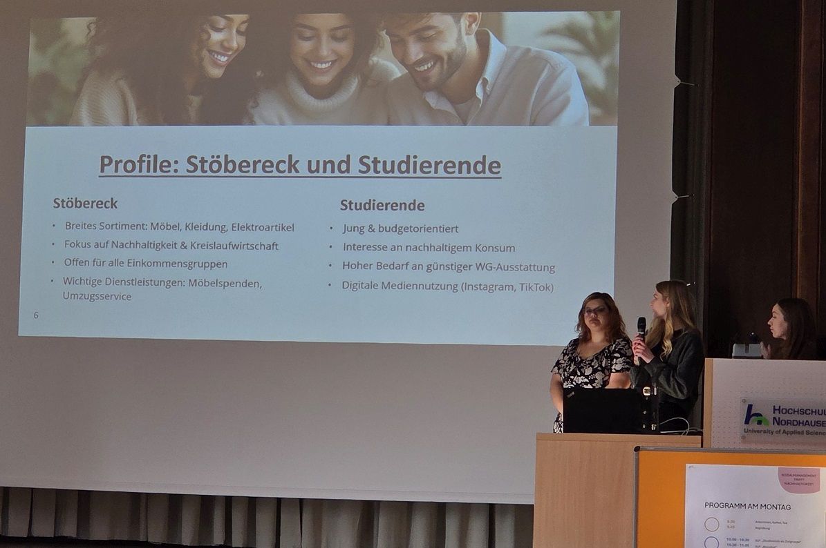 Three young women present in front of a slide with the profiles „Stöbereck“ and „Studierende“, on which topics such as budget orientation, sustainability and furniture donations are described.