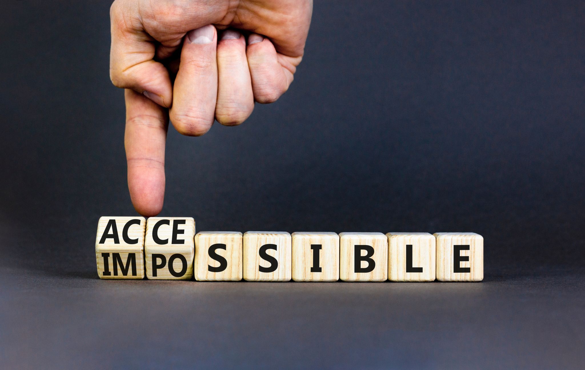 Hand points to the word "ACCESSIBLE" made up of letter cubes, the first cube is tilted, if you turn it over, "IMPOSSIBLE" appears instead"