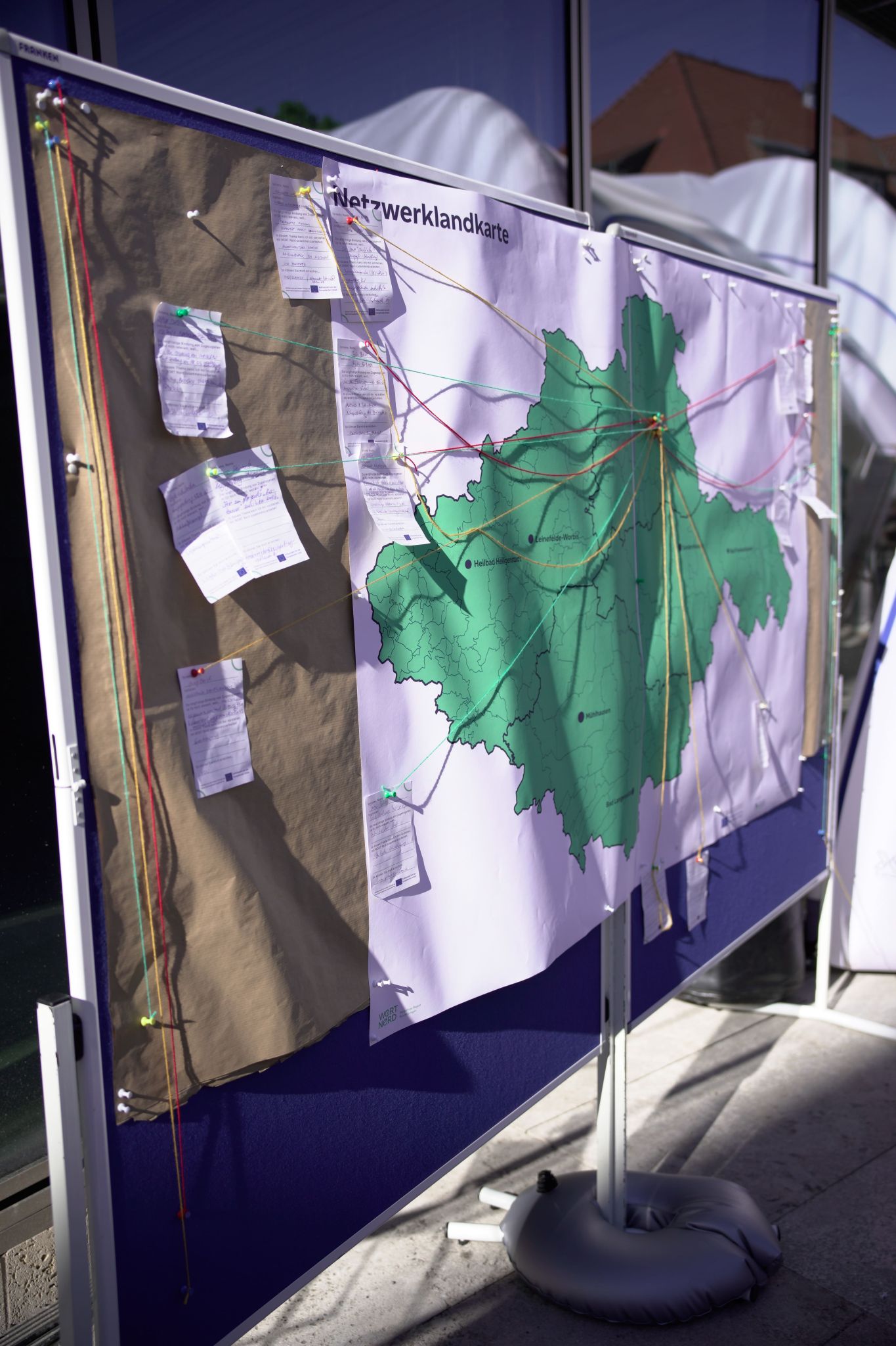 A noticeboard featuring a network map displays a map of the region, sticky notes and coloured threads linking various locations and stakeholders. This interactive visualisation serves to highlight existing networks and collaborations within the context of a participatory or research event.